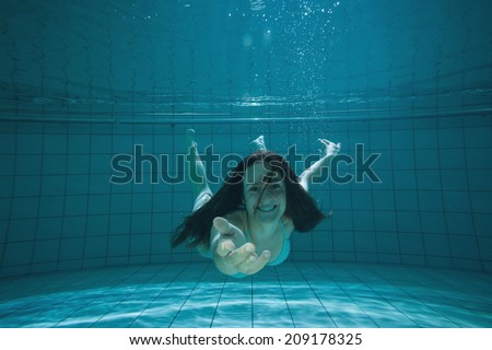 Pretty brunette smiling and offering her hand underwater in the swimming pool at the leisure centre