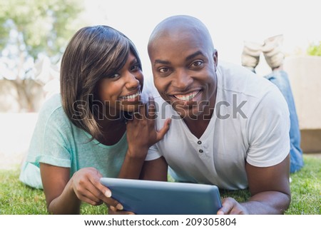 Happy couple lying in garden using tablet pc together on a sunny day