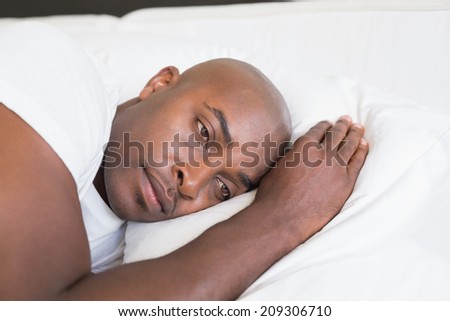 Unhappy man lying in bed at home in the bedroom