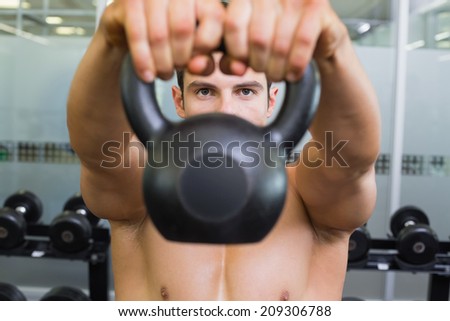 Portrait of a young muscular man lifting kettle bell in gym