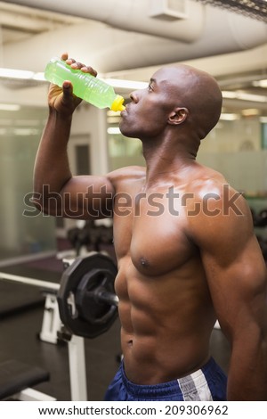 Shirtless muscular man drinking energy drink in gym