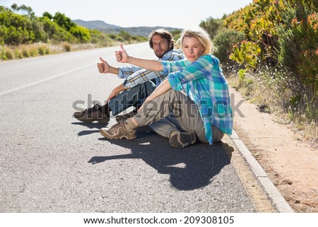 Attractive couple sitting on the road hitching a lift on a sunny day