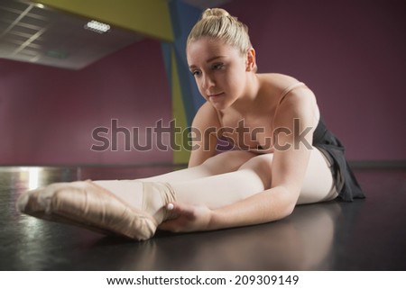 Ballerina sitting and bending forward in the ballet studio