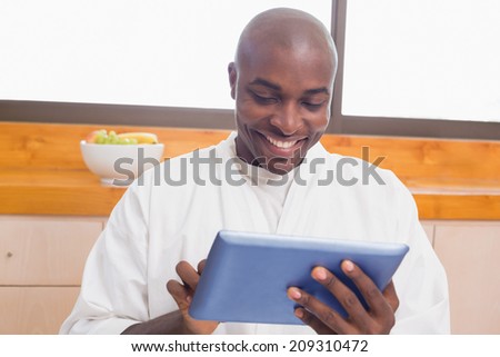 Happy man in bathrobe using tablet pc at home in the kitchen