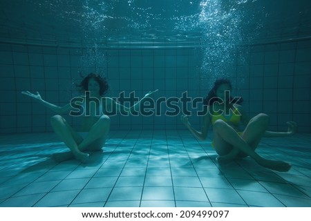 Pretty friends sitting underwater in bikinis in the swimming pool at the leisure centre