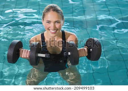 Fit blonde working out with foam dumbbells in swimming pool at the leisure centre
