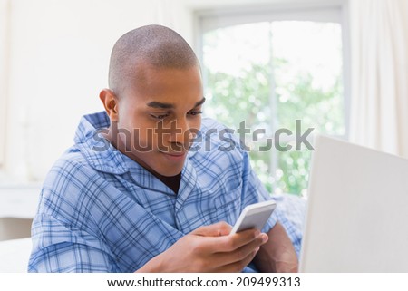 Happy man using laptop on bed and texting at home in the bedroom