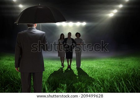 Mature businessman holding an umbrella against football pitch with bright lights