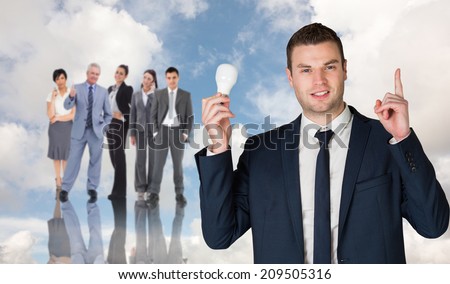 Businessman holding light bulb and pointing against blue sky with white clouds