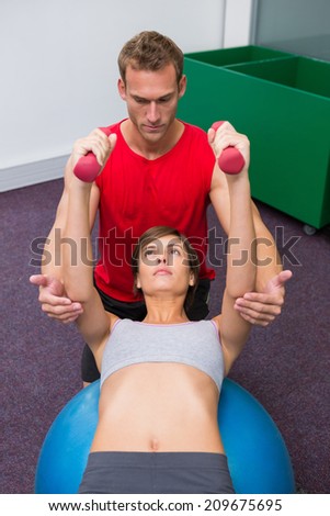 Personal trainer with client lifting dumbbells on exercise ball at the gym