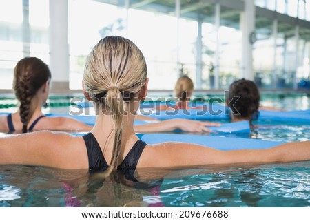 Female fitness class doing aqua aerobics with foam rollers in swimming pool at the leisure centre