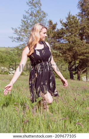 Pretty blonde in sundress walking through field on a sunny day in the countryside