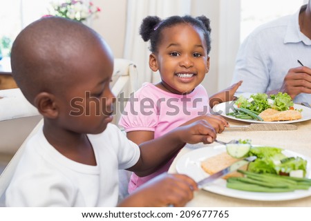 Family enjoying a healthy meal together with daughter smiling at camera at home in the kitchen