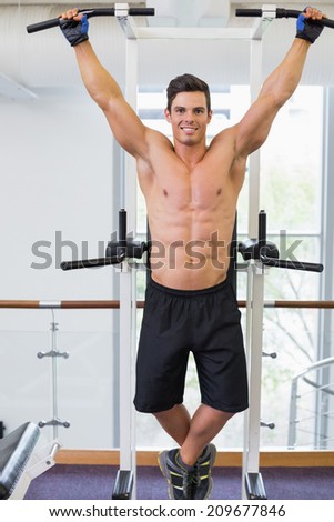 Shirtless male body builder doing pull ups at the gym