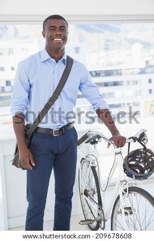Happy businessman standing with his bike in his office