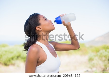 Fit woman drinking water from sports bottle on a sunny day in the countryside