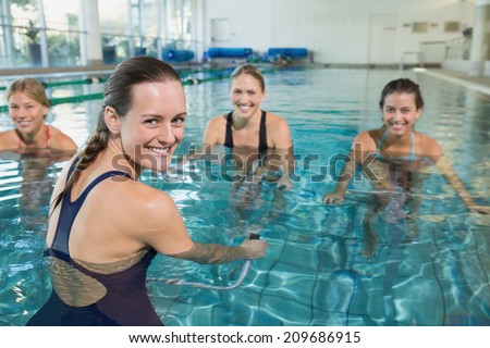 Female fitness class doing aqua aerobics on exercise bikes in swimming pool at the leisure centre