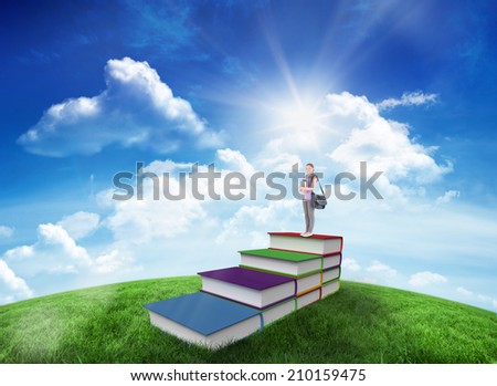 Attractive student holding books and her bag while standing against green hill under blue sky