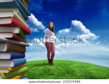 Smiling student holding textbook against green field under blue sky