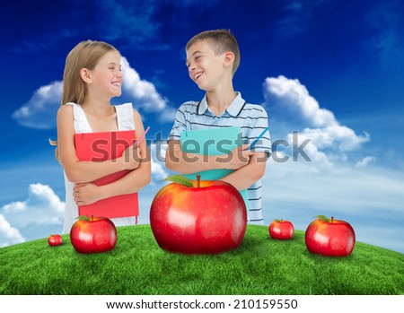 Smiling brother and sister holding their exercise books against green field under blue sky