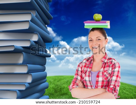 Pretty student holding an apple and books on her head against green field under blue sky