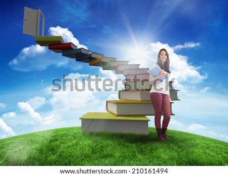 Smiling student holding textbook against green hill under blue sky