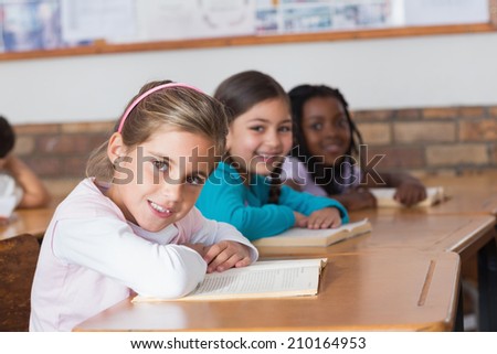 Cute pupils reading books at their desks at the elementary school