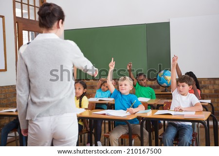 Cute pupils raising their hands in class at the elementary school