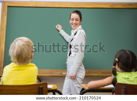 Pretty teacher writing on chalkboard at the elementary school