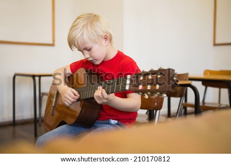 Cute pupil playing guitar in classroom at the elementary school