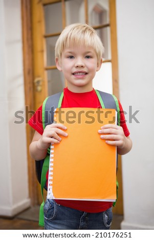 Cute pupil smiling at camera in classroom holding notepad at the elementary school