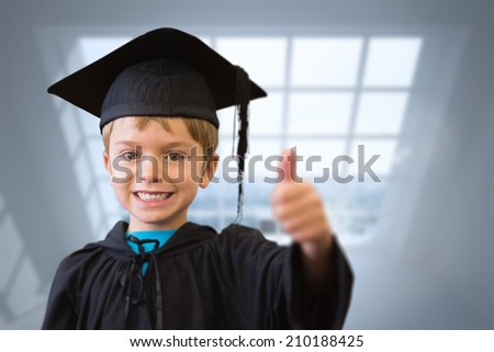 Cute pupil in graduation robe against room with large windows showing city