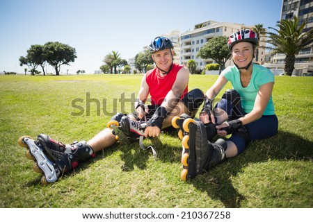 Fit mature couple tying up their roller blades on the grass on a sunny day