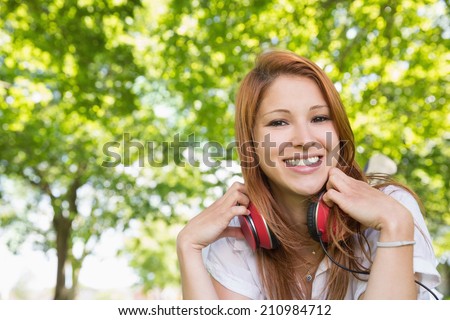 Pretty redhead listening to music in the park on a sunny day