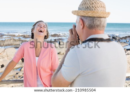 Happy casual man taking a photo of partner by the sea on a sunny day