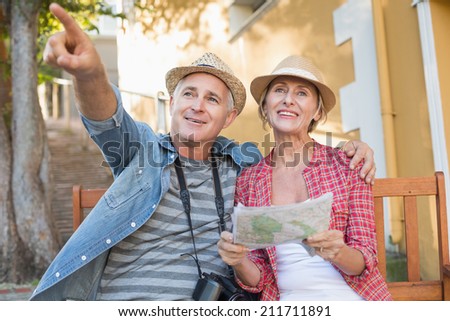 Happy tourist couple looking at map on a bench in the city on a sunny day