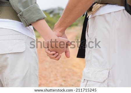 Rear view close up of hiking couple holding hands on mountain terrain