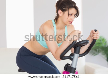 Fit brunette working out on exercise bike at home in the living room