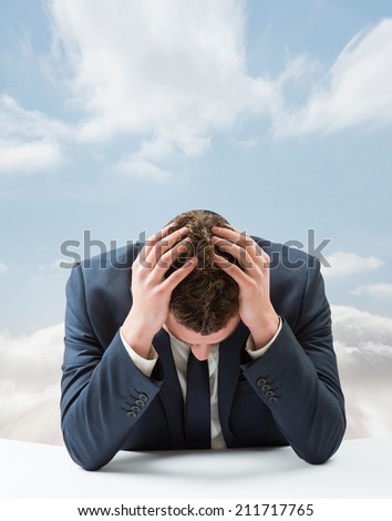 Businessman with head in hands against cloudy sky
