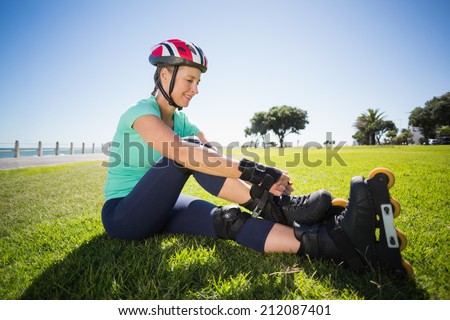Fit mature woman tying her roller blades on the grass on a sunny day