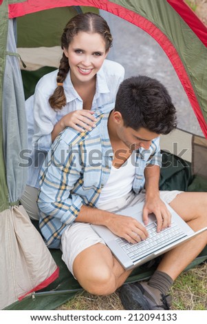 Young couple using laptop in tent on countryside landscape