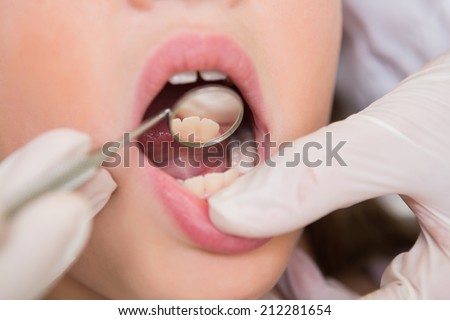 Pediatric dentist examining a little girls teeth in the dentists chair at the dental clinic