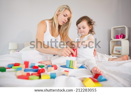 View of mother and daughter playing with building blocks on bed at home