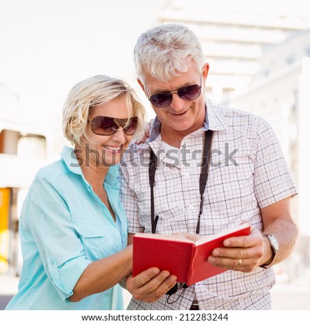 Happy tourist couple using tour guide book in the city on a sunny day