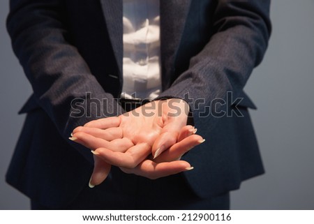 Businesswoman in suit holding her hands out on grey background