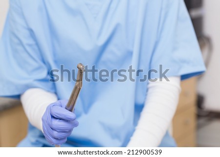 Dentist in blue scrubs holding dental drill at the dental clinic