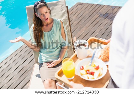 Upset young woman looking at cropped waiter with breakfast tray by the pool