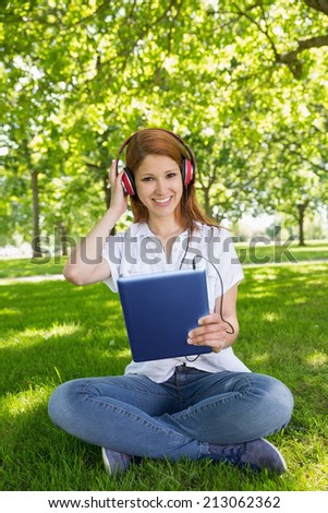 Pretty redhead using her tablet pc while listening to music in the park on a sunny day