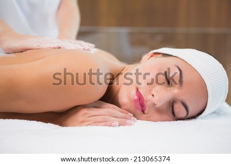 Close up of an attractive young woman receiving back mask cream at spa center