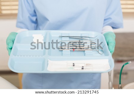 Dentist in blue scrubs holding tray of tools at the dental clinic